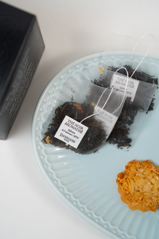 Cup of Jardin Bleu black tea with Dammann Frères tea box, tea sachets and biscuit.