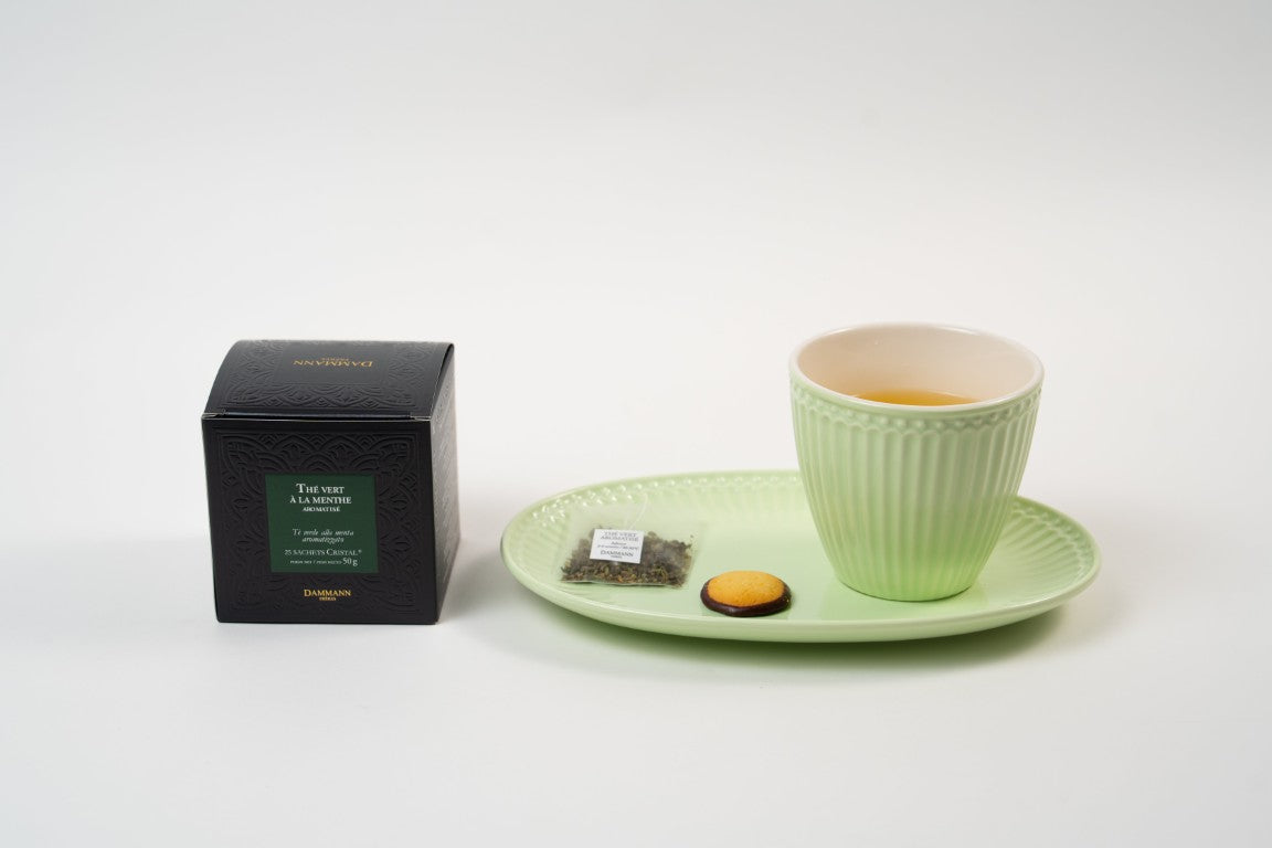 Dammann Frères mint green tea with teacup, tea sachet and biscuit on green plate.