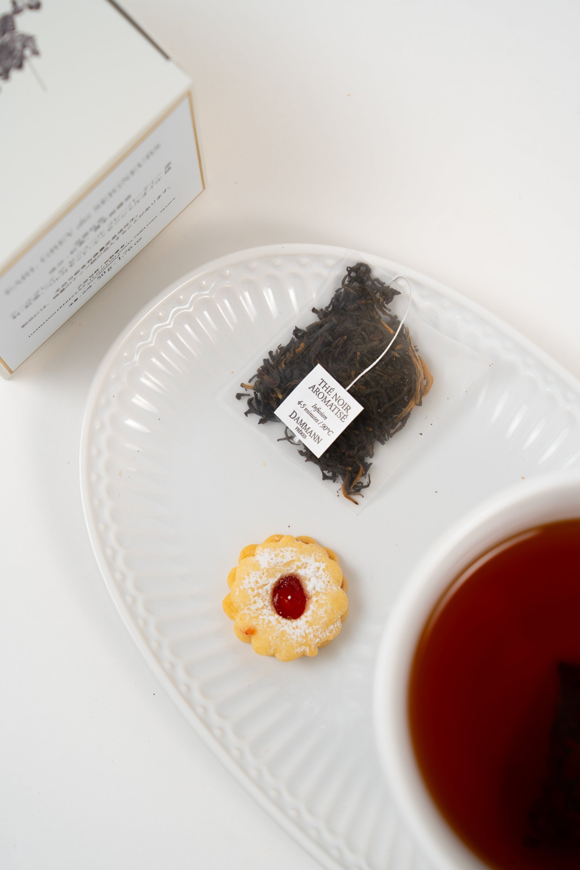 Dammann Frères Romes black tea sachet served with brewed tea and delicate biscuit on elegant white porcelain