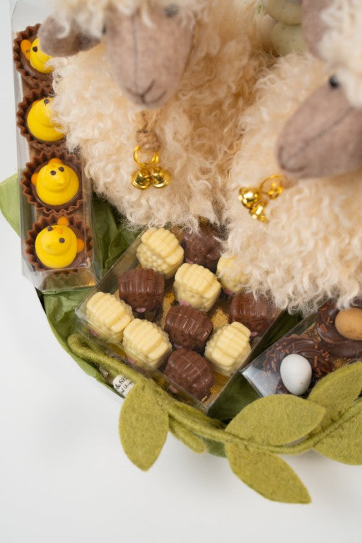 Close-up of decorative plush lamb with bell surrounded by Easter chocolates and pralines.
