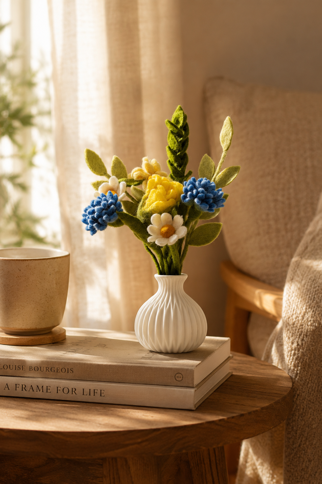 Handmade felt flower bouquet in a white ceramic vase styled on a wooden side table in a warm cosy interior with soft natural light.