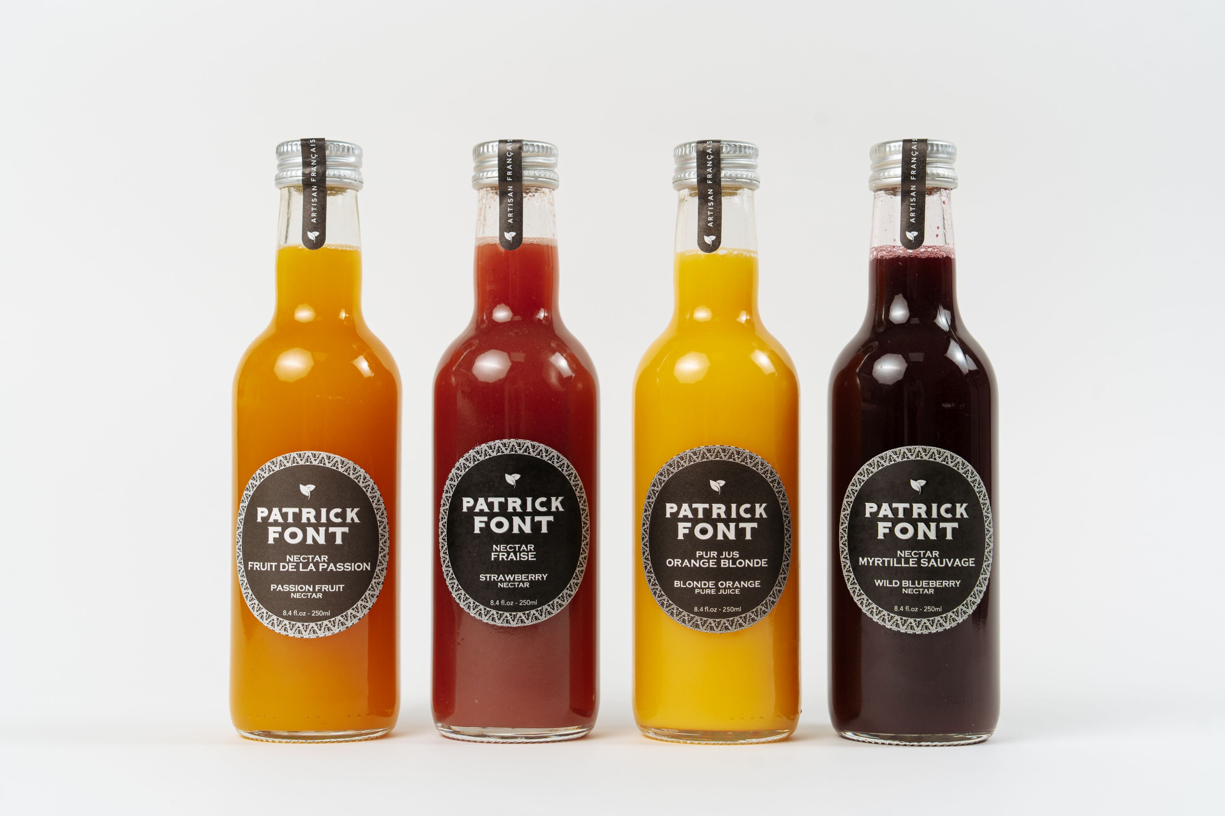 Assortiment de jus et nectars de fruits artisanaux en bouteilles, incluant orange, fraise, fruit de la passion et myrtille