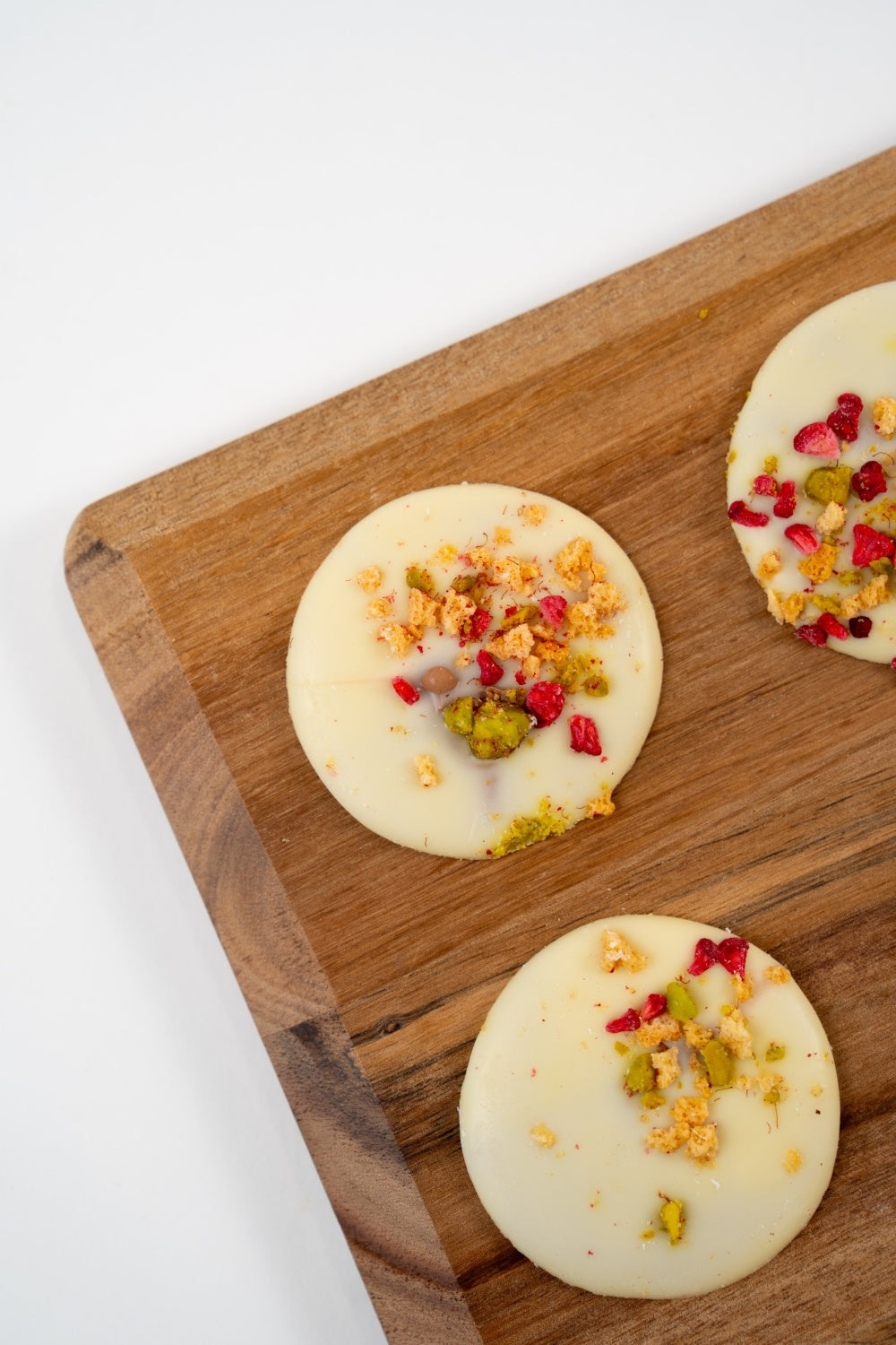 Belgian white chocolate mendiant topped with pistachios and freeze-dried raspberry on a light background.
