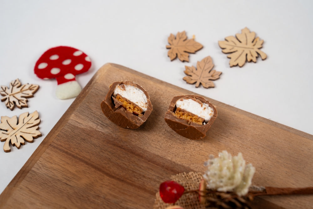 Mini Melocake Brésilienne au chocolat au lait coupé en deux, révélant une guimauve blanche et un cœur croustillant doré, présenté sur une planche en bois avec des décorations automnales.