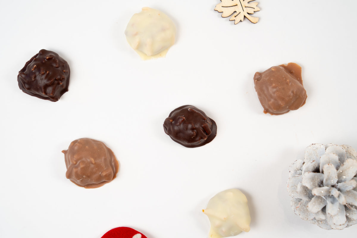 Assortiment de mini Weichprinten aux noisettes enrobés de chocolat blanc, au lait et noir, présenté sur fond blanc.