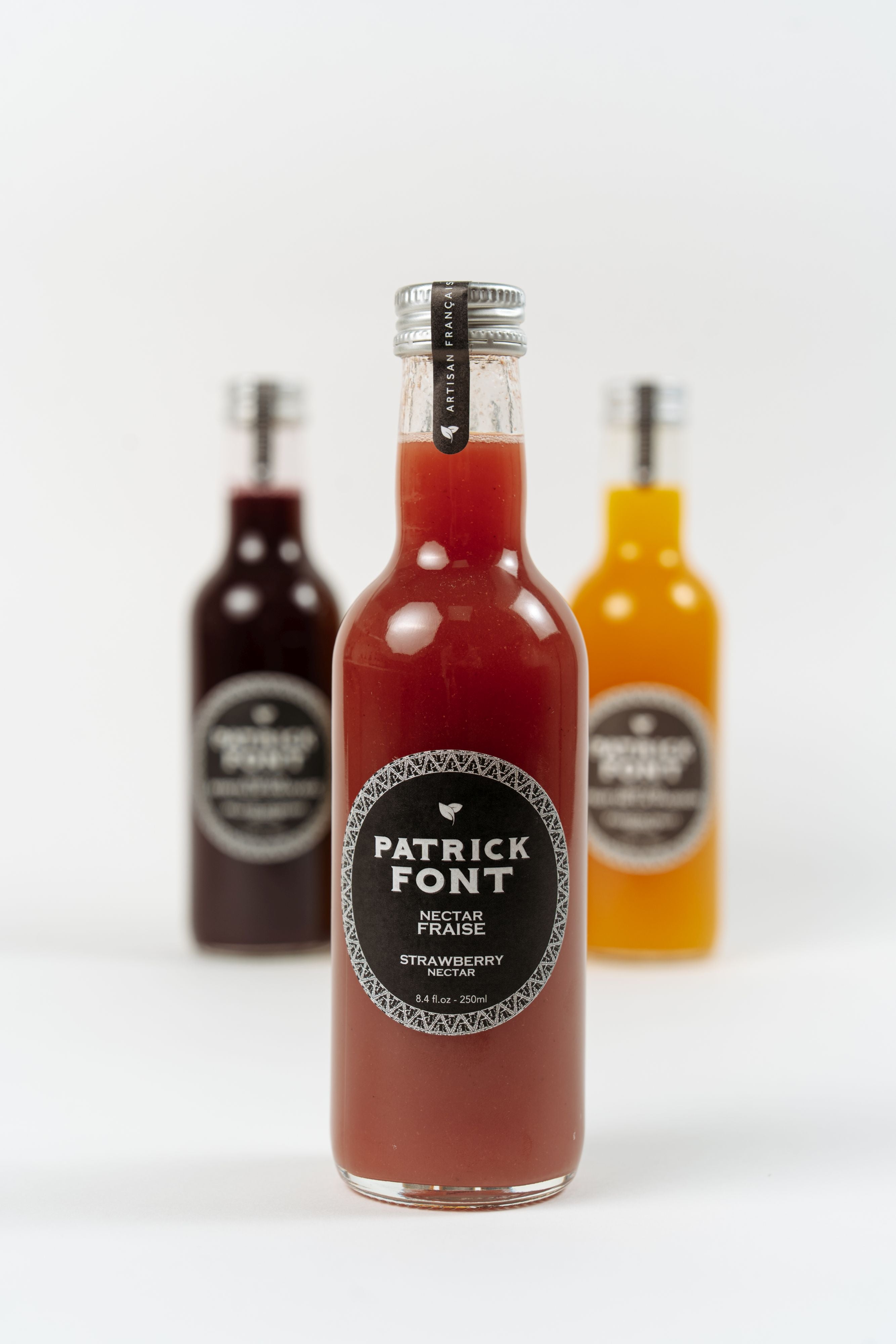 Bouteille de nectar de fraise Patrick Font avec bouteilles de nectar en arrière-plan.