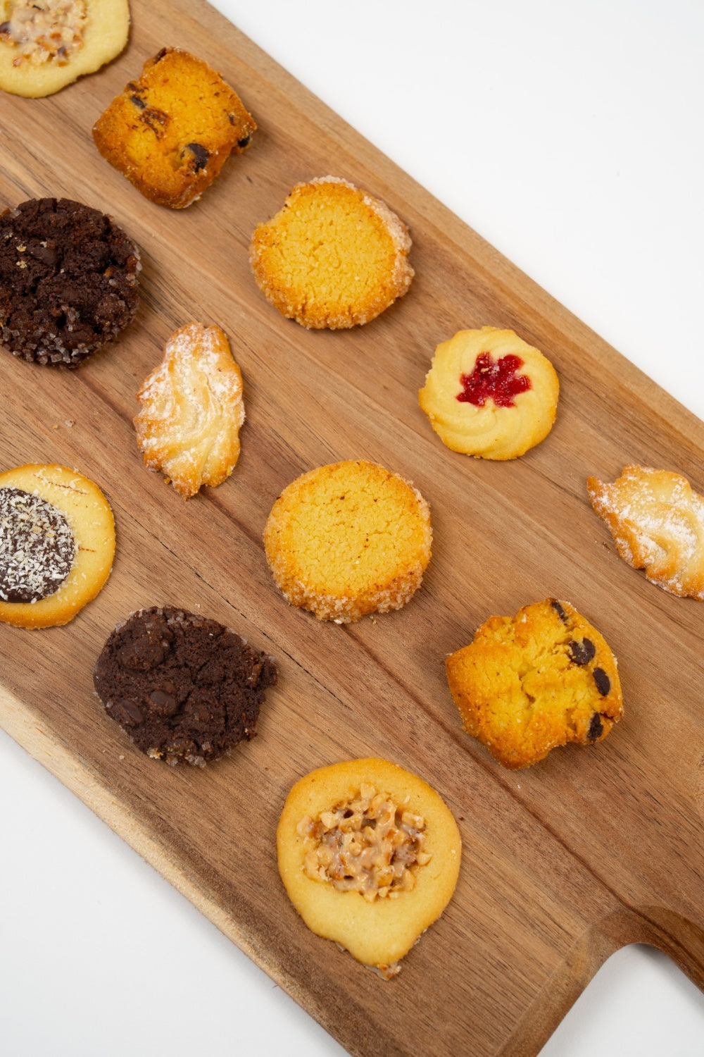 Biscuits variés de l’Assortiment de Biscuits Artisanaux Péché Mignon disposés sur une planche en bois, dont certains partiellement cadrés.