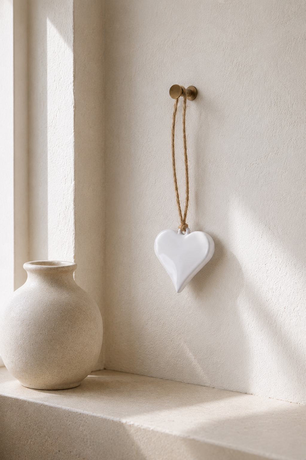 White ceramic heart hanging decoration styled on a textured wall with soft natural light.