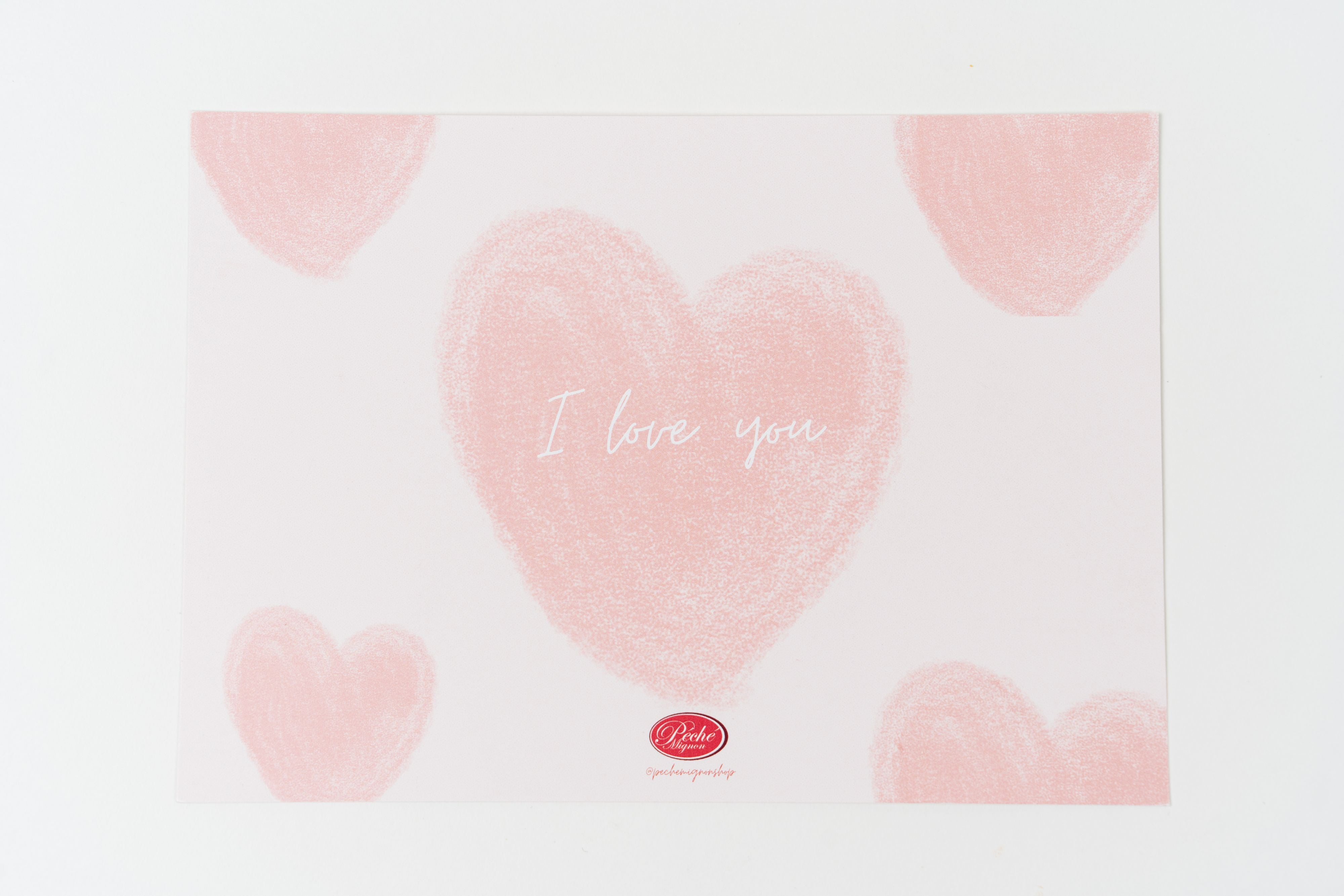 Romantic Péché Mignon greeting card with soft pink heart illustrations and “I love you” text on a white background.