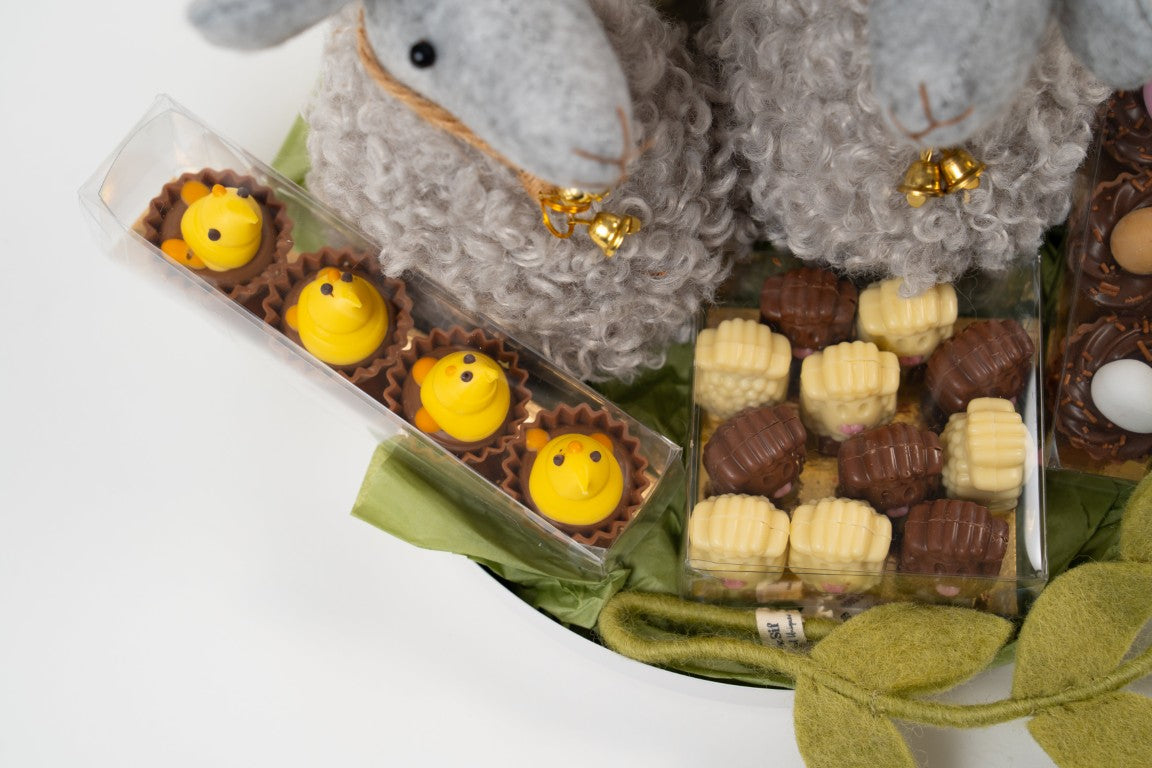 Easter chocolate assortment with two grey lamb decorations, mini chocolate eggs and pralines on a festive platter.