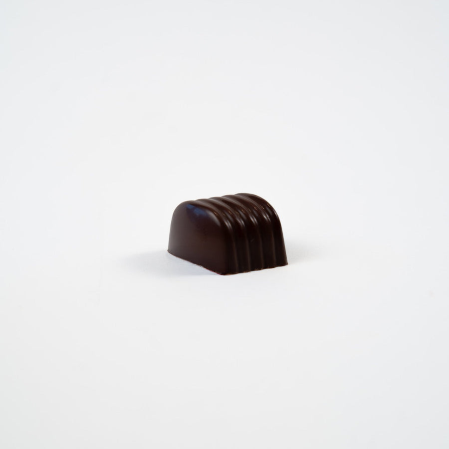 Artisan Belgian Paola praline in dark chocolate with fresh cream and pistachio, on a white background.