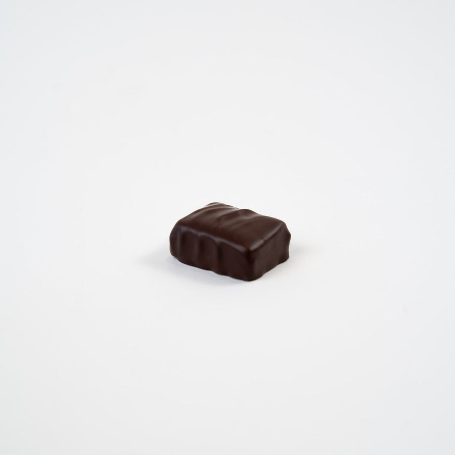 Artisan Belgian Pistou praline in dark chocolate with pistachio marzipan, on a white background.