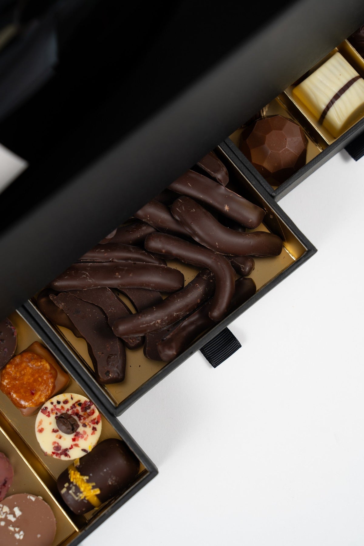 Vue rapprochée des tiroirs de pralines artisanales assorties et d’orangettes au chocolat noir