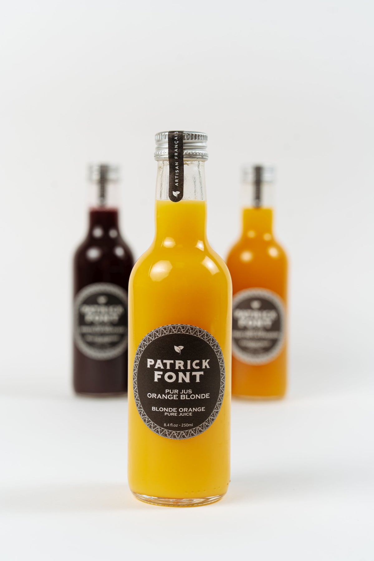 Bouteille de pur jus d’orange blonde Patrick Font avec bouteilles de jus en arrière-plan.