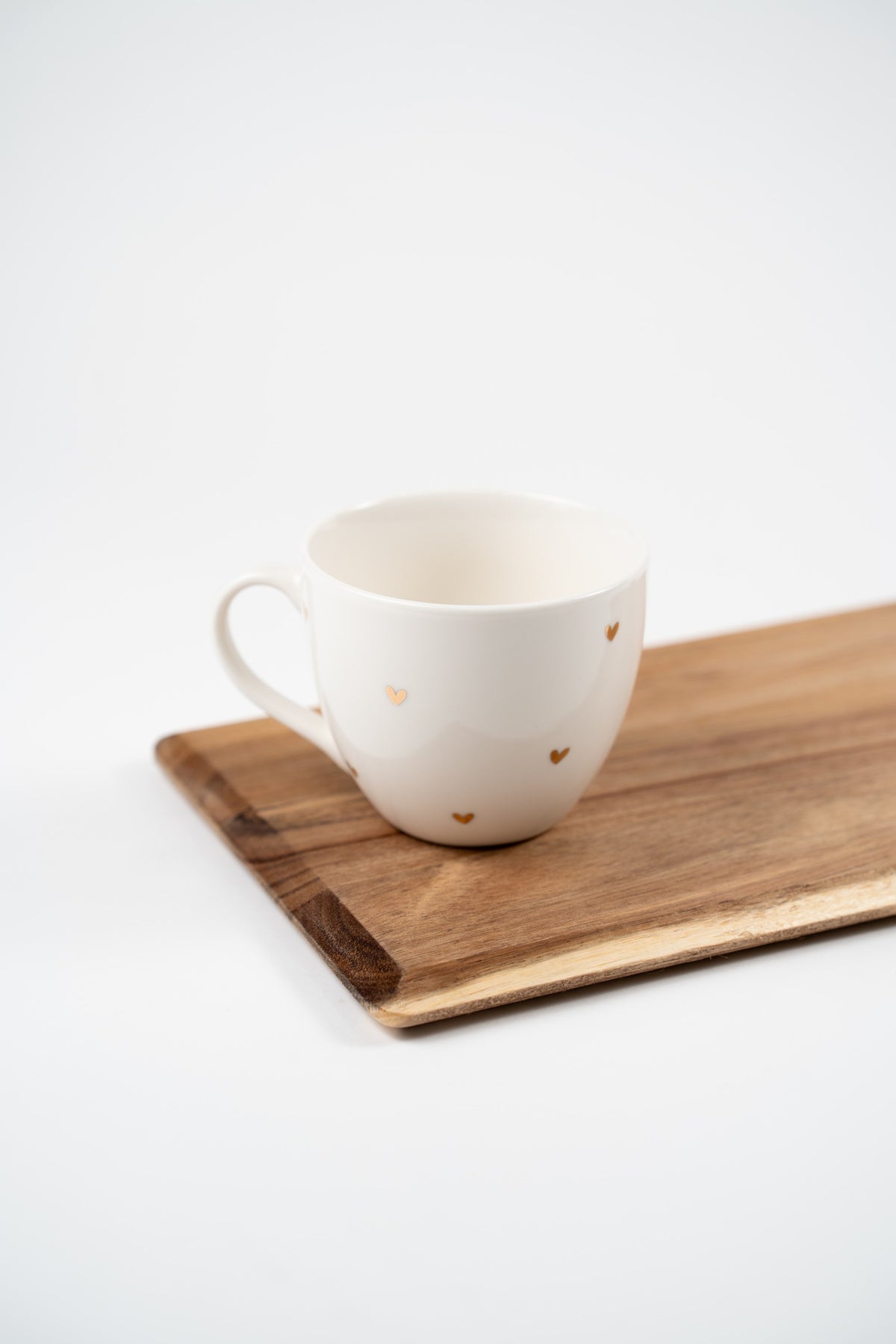 Taza grande de porcelana blanca de 420 ml, decorada con pequeños corazones dorados y colocada sobre una tabla de madera.