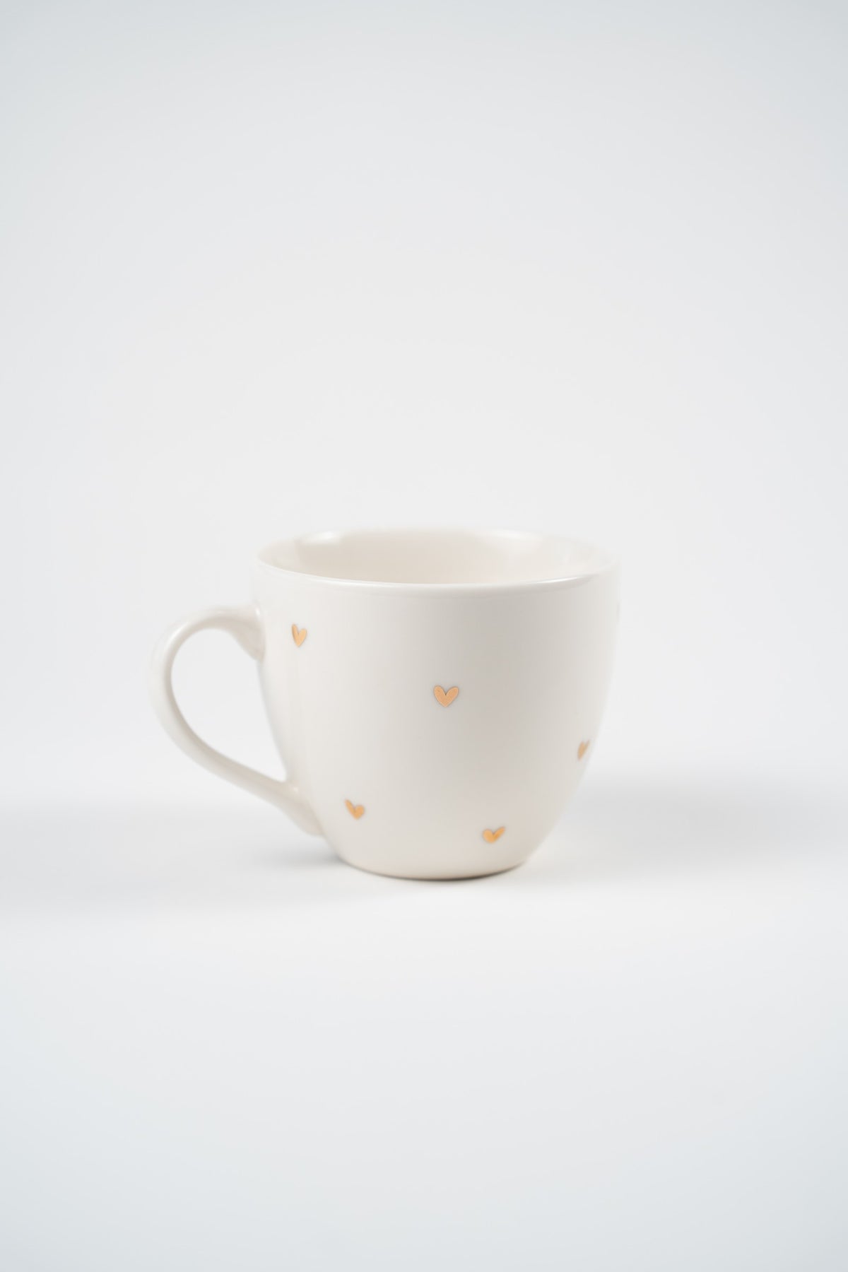 Taza de porcelana blanca de 420 ml con pequeños corazones dorados, vista de frente con su asa redondeada.