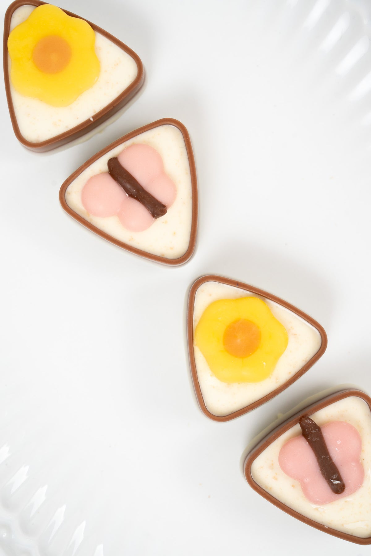 Triangular chocolate pralines decorated with flower designs on a white plate