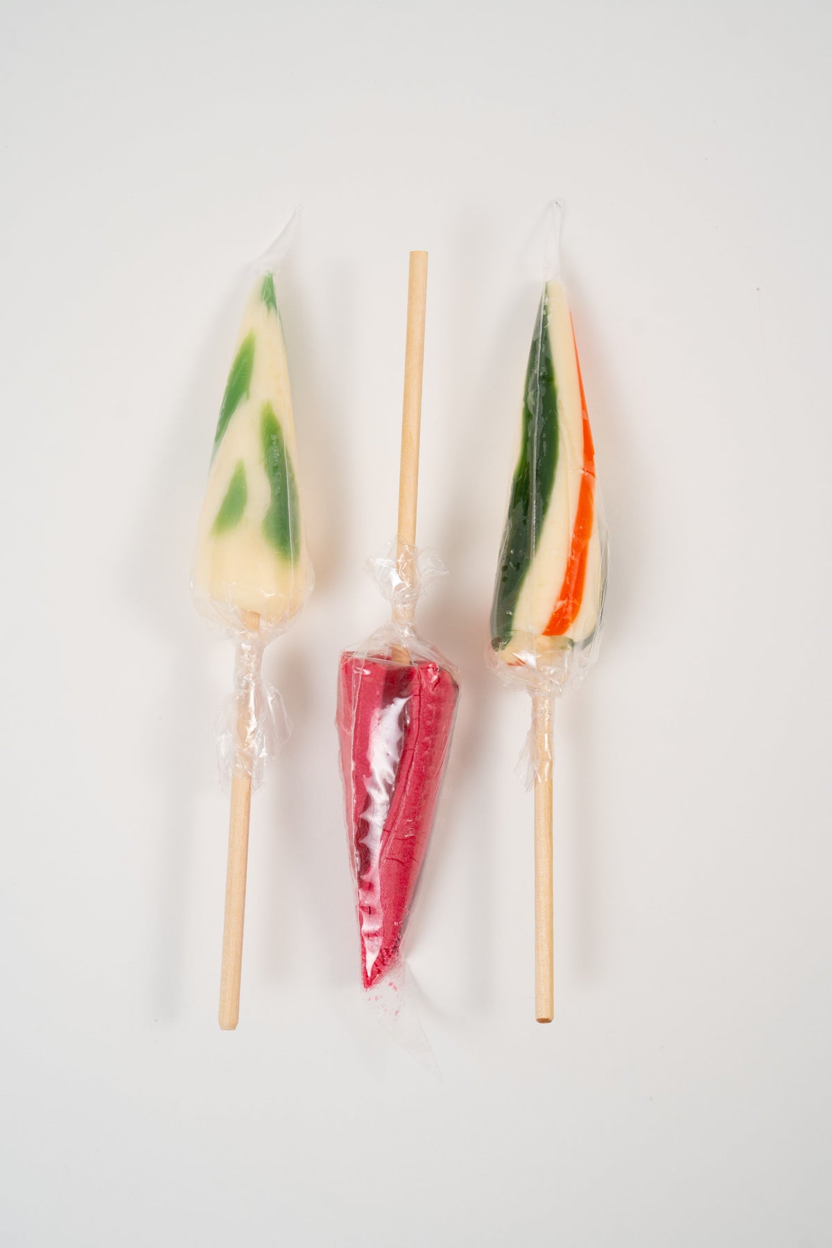 Sélection de trois sucettes en forme de parasols aux saveurs orange, fraise et fleur de sureau.