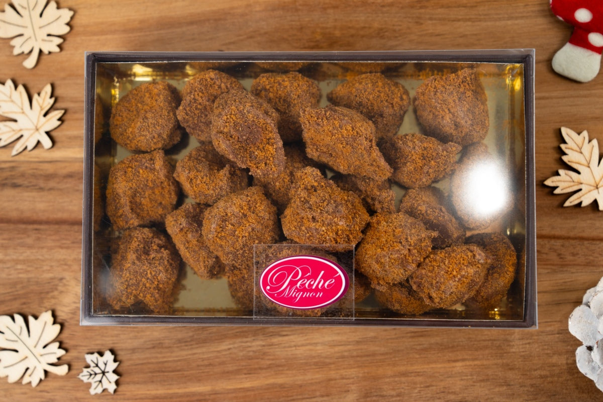 Coffret de 300 g de truffes belges au spéculoos, visible à travers un couvercle transparent sur une planche en bois.