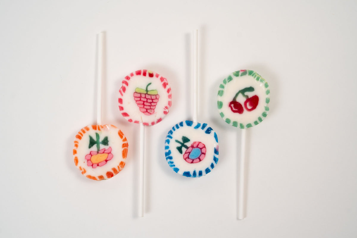 Assortiment de quatre sucettes artisanales colorées avec motifs de cerise, framboise et fleurs.